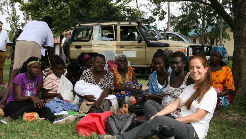 Cristina Sansalvador and Kenyan woman sitting on the grass at a mother-to-mother outreach, smiling into the camera.  