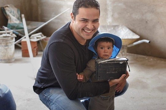 Fernando Sepulveda smiling into the camera with a Bolivian child.