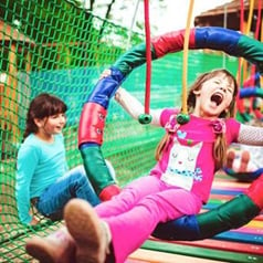 Děti hající si na dětském hřišti. V popředí výskající holčička v barevné obruči.