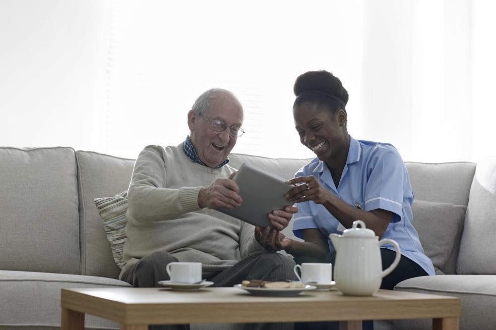 Female nurse and male patient sitting on the couch looking at a tablet and laughing
