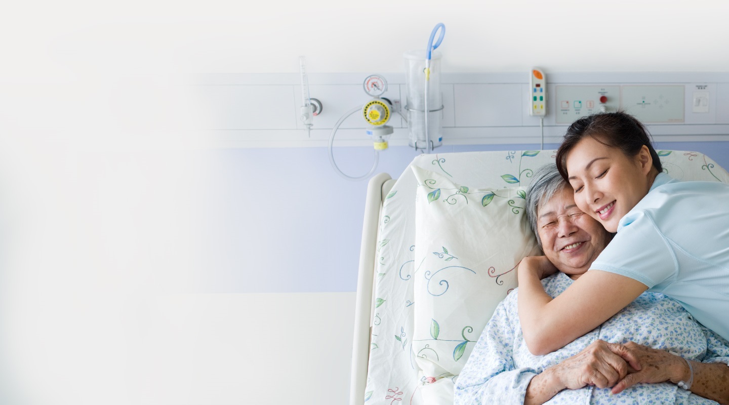 Hastane yatağında yatan bir kadın hastayı kucaklayan hemşire - ikisi de gülümsüyor