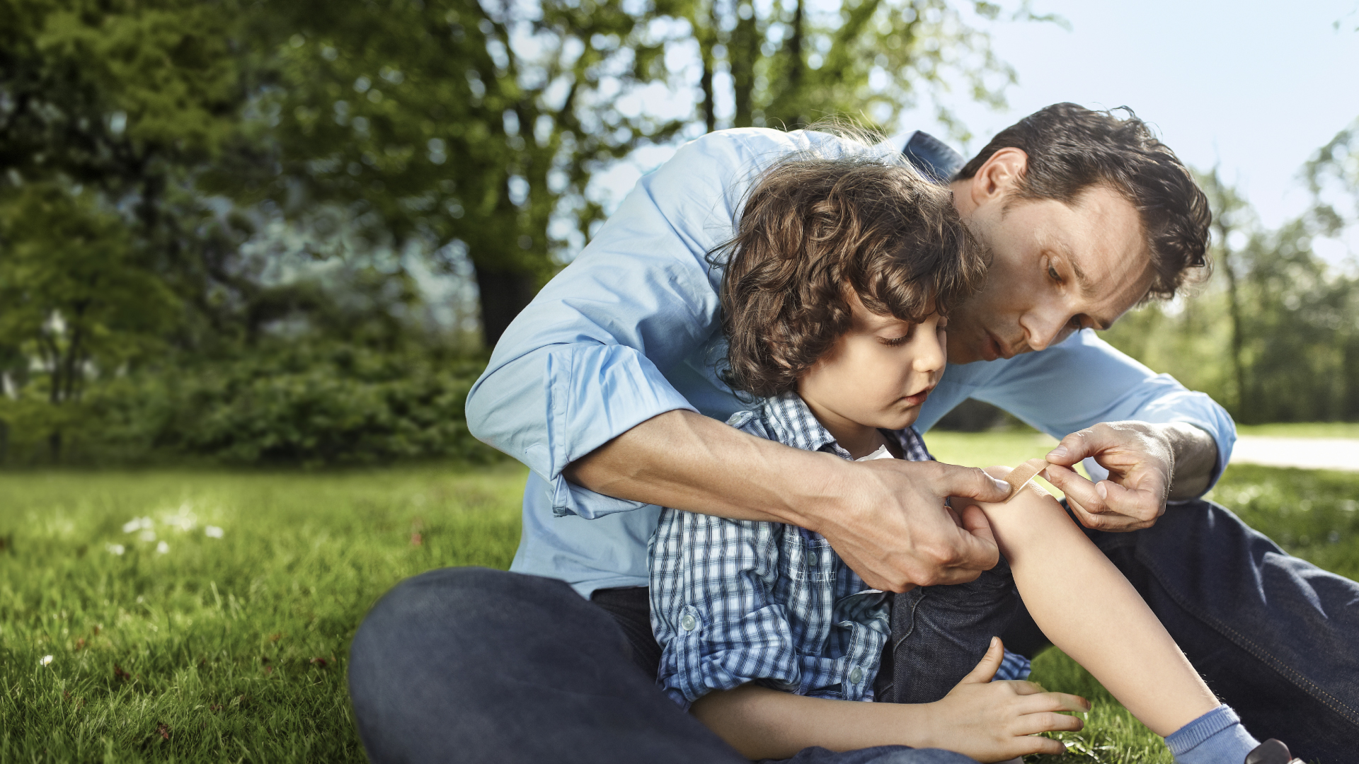 A father covering his son's graze with a plaster.