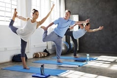 Man in a blue t-shirt trying to do yoga with two women