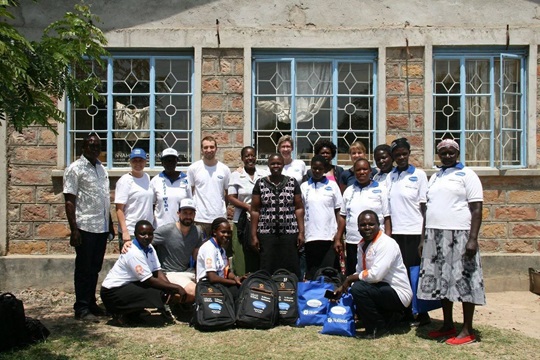 Members of the Kisumu community and HARTMANN volunteers standing in front of a building smiling into the camera.