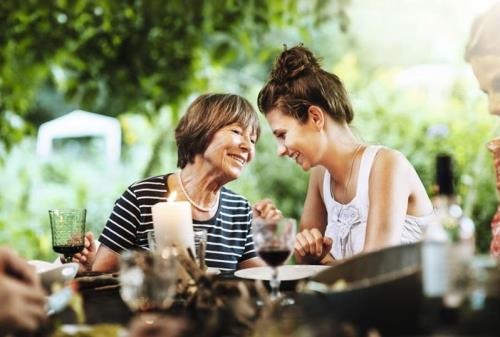 An elderly and young woman sitting outside at a table talking and laughing.