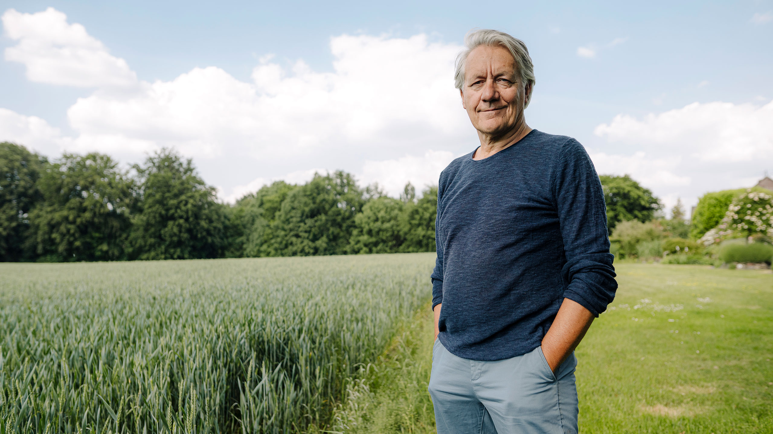 Un hombre de pie mirando a cámara en un campo de trigo verde