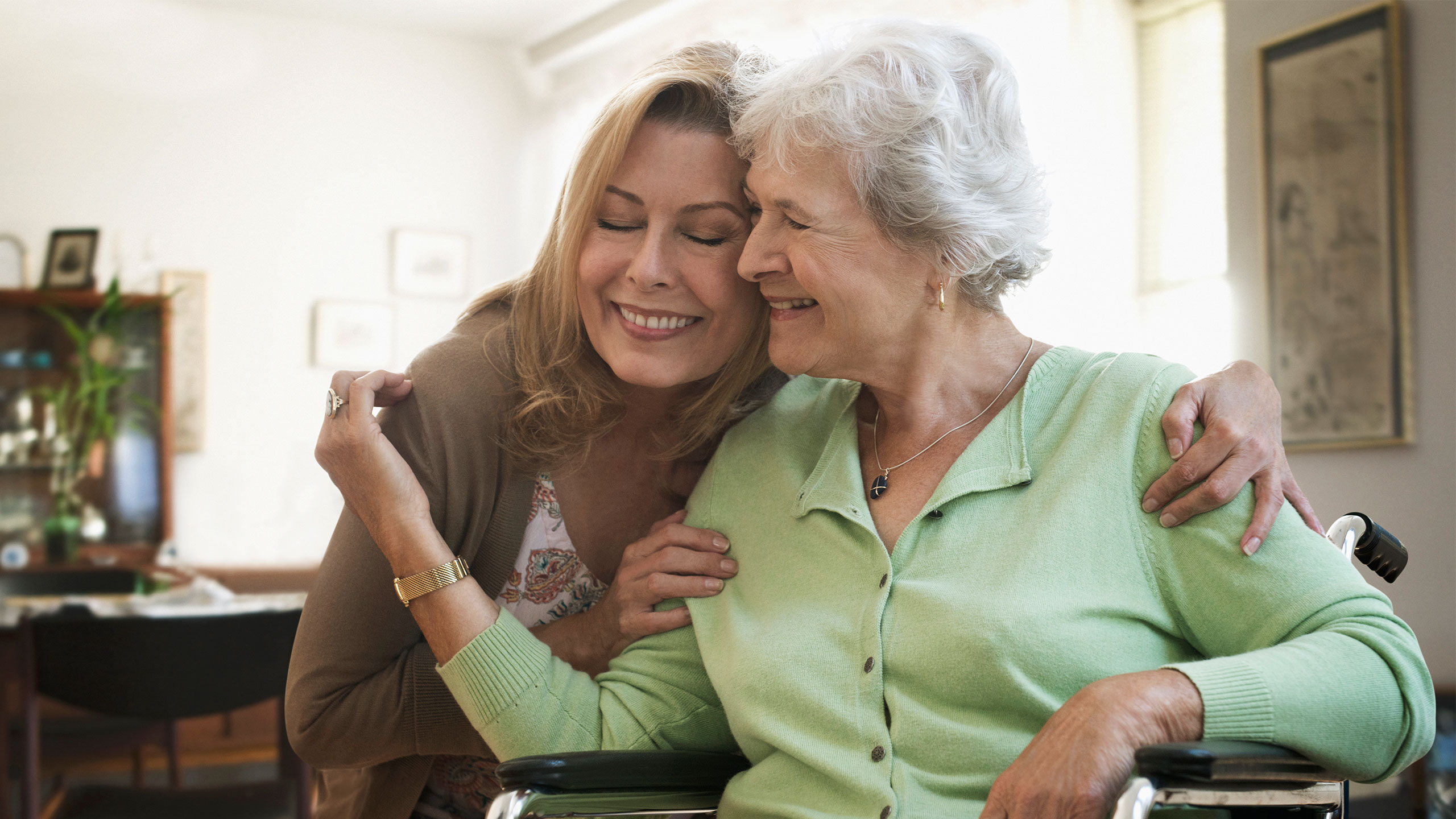 A young woman is hugging an older woman who is sitting in a wheelchair. 