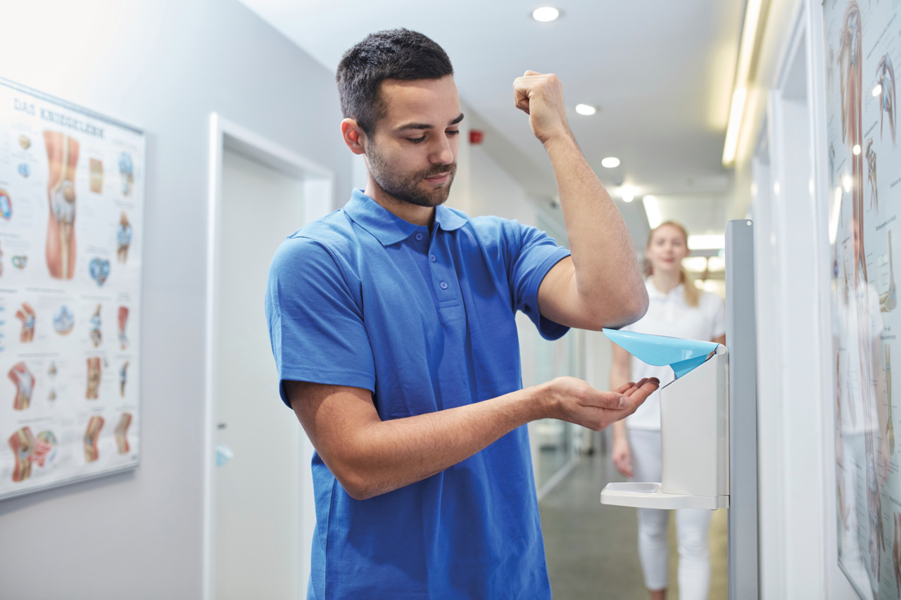 Un enfermero realizando una desinfección de manos con un dispensador de pared en el pasillo de un hospital