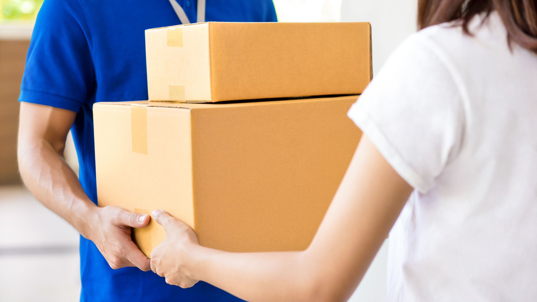 Kurýr v modré košili předává dvě kartonové krabice – doručení balíčku domů pro jednotlivce.