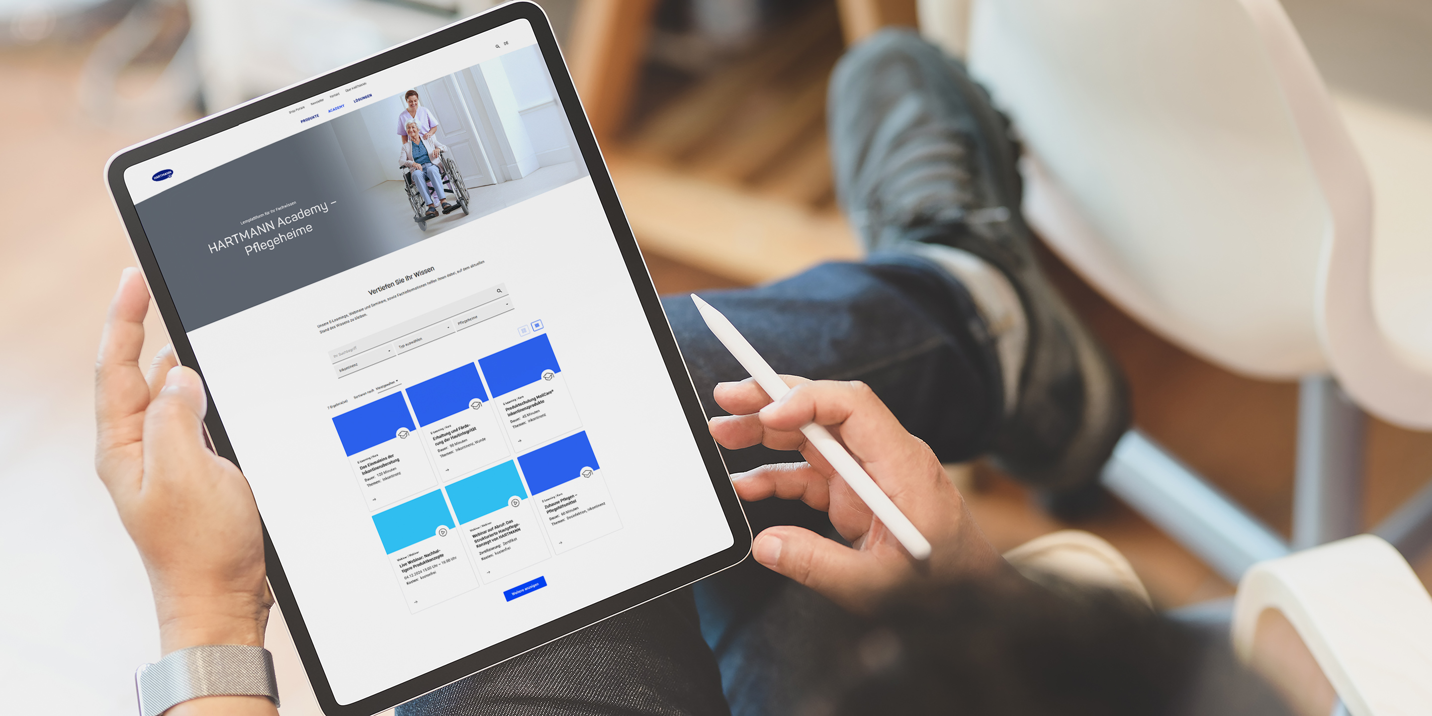 Tablet liegt auf dem Knie eines Mannes und zeigt die Startseite der HARTMANN Academy für Pflegeheime