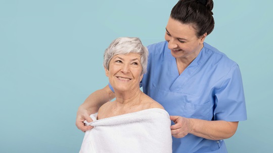 Eine Krankenschwester hilft einer älteren Frau, während sie ihr ein Handtuch reicht und sie freundlich anlächelt