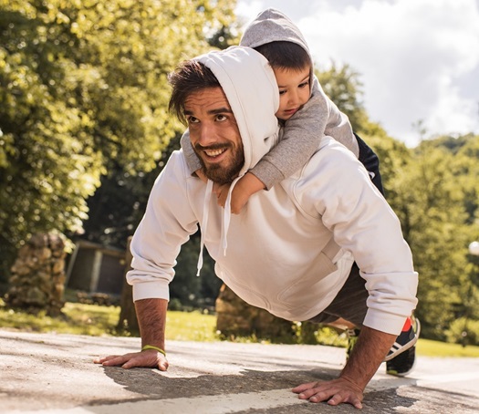 A young father exercising push-ups with his son on his back.