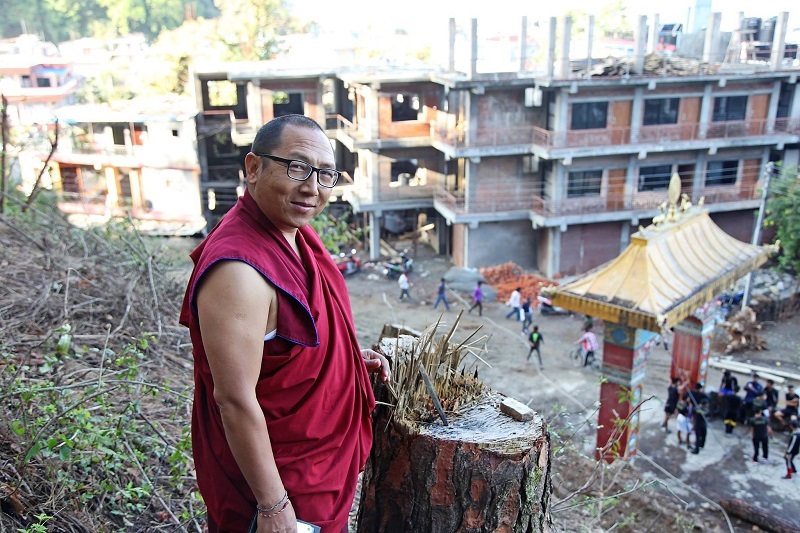 Image of monk and Buddhist master Mukhya Gurung in front of school.