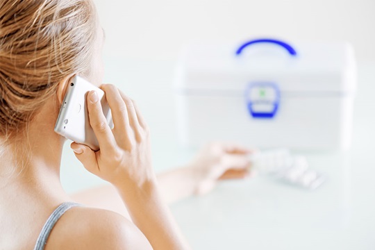 Woman holding mobile phone to ear while opening first aid box.