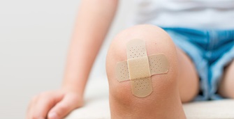 Child sitting wearing blue jeans short with two plasters as cross on knee.