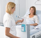 Patient lying in her bed, smiling at the doctor’s assistant, while the assistant is disinfecting her hands.