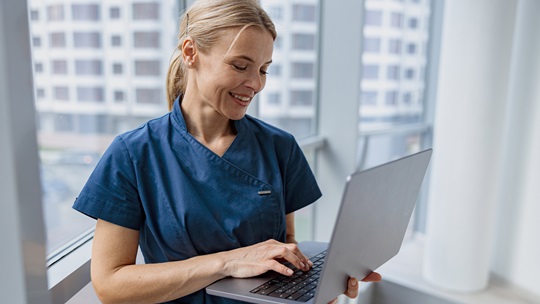 Pflegerin / Ärztin im Flur schaut in einen Laptop