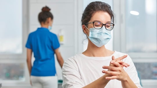 Frau mit Mundschutz verreibt die Händedesinfektion