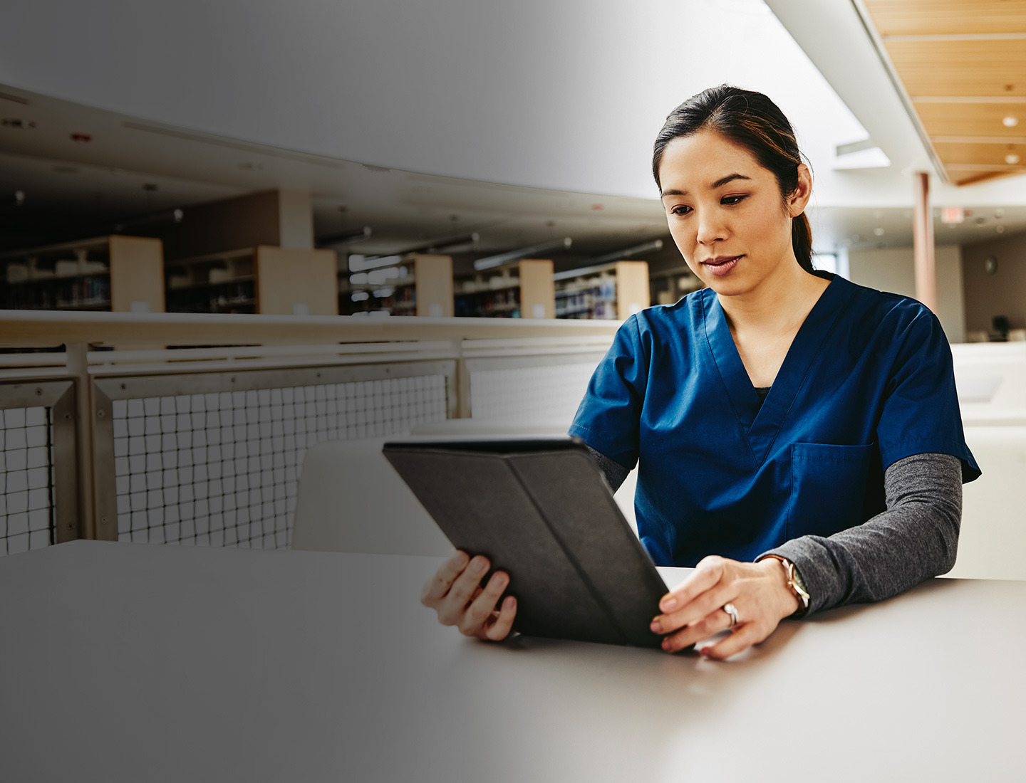 Woman in a tunic sits at the table and looks into a tablet