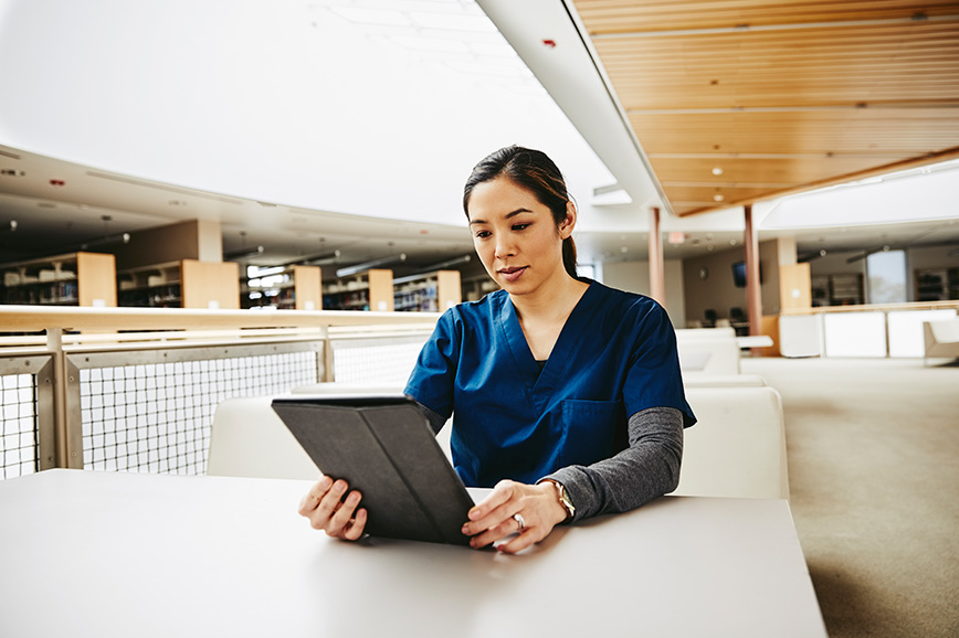 Woman in a tunic sits at the table and looks into a tablet