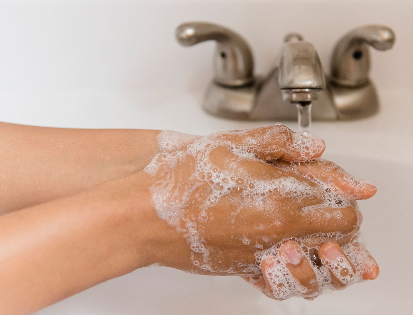 A woman is washing her hands at a sink.