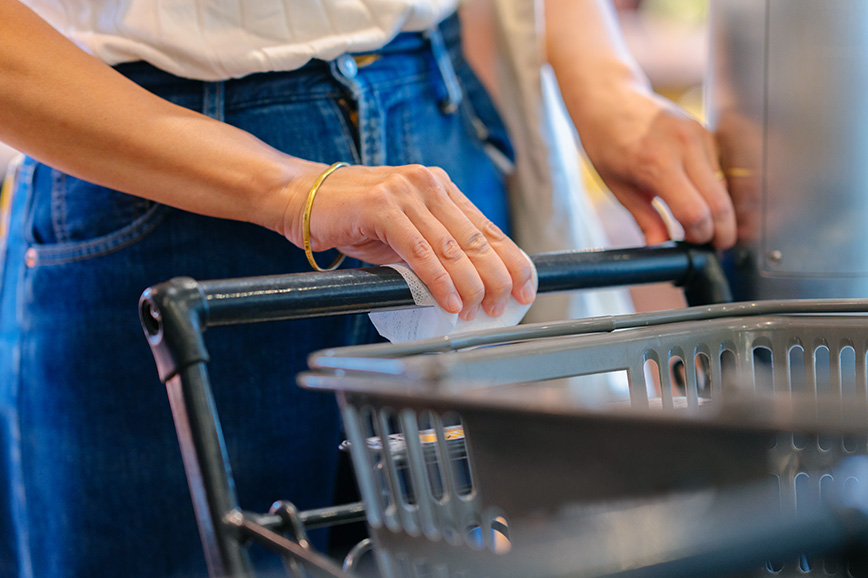 A woman is disinfecting the handle of a shopping trolley.