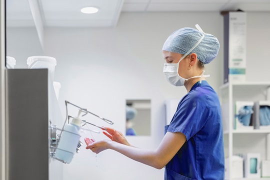 Nurse in surgical scrubs disinfects her hands.