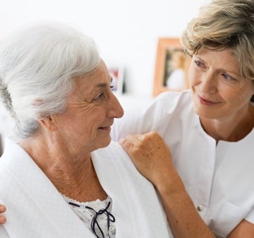 A women, dressed in a nurse’s coat is taking care for an elderly woman