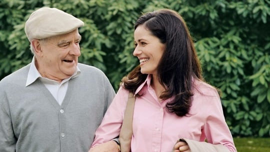A young woman and an old man are walking together in a park.