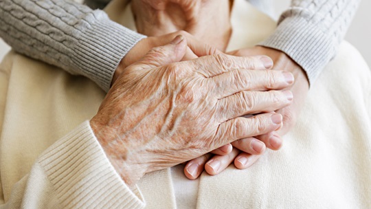 Seniorenhand und jüngere Hand liegen aufeinander vor der Brust der Seniorin