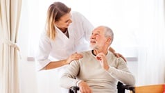 Pflegerin schaut Senior im Rollstuhl von hinten über die Schulter