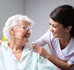 Seniorin mit Pflegerin lachend auf dem Sofa