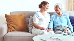 Pflegerin mit Seniorin auf Sofa