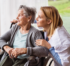 Seniorin im Rollstuhl schaut mit Pflegerin zum Fenster raus