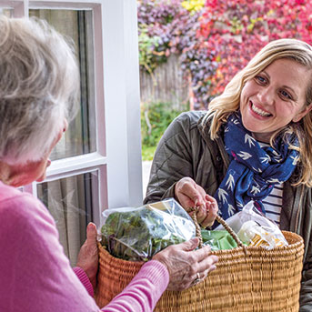 Nachbarin übergibt Seniorin Einkaufskorb an der Haustür