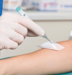 Aufbringen einer Wundabdeckung am Arm mittels Peha-Instrument Pinzette