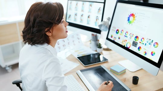 Business Frau sitzt vor zwei Monitoren mit Analysedaten