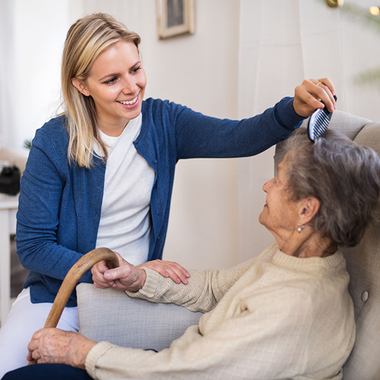 Junge Frau kämmt Haare einer Seniorin