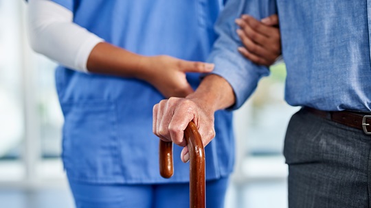 Pflegerin führt Senior mit Stock am Arm