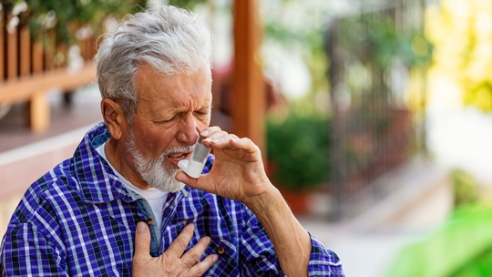Senior trinkt ein Glas Wasser und hält sich die Hand an die Brust