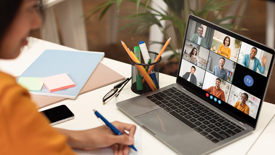 Frau sitzt mit Stift und Block vor Laptop bei einem online Meeting