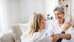 Pflegerin spricht mit Seniorin im Sessel