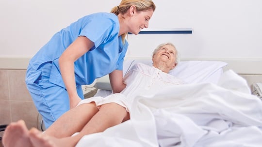 Pflegerin lagert Seniorin im Bett um