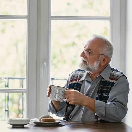 älterer Mann sitzt am Tisch und hält eine große Tasse in der Hand