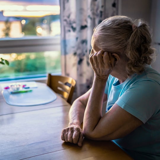 ältere Frau sitzt am Tisch und schaut aus dem Fenster