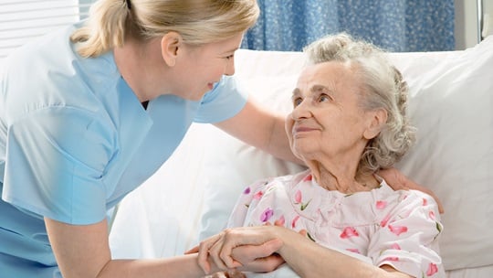 Pflegerin beugt sich über Seniorin, die im Bett liegt
