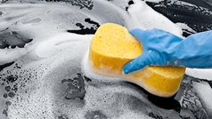 Hand mit Schwamm wäscht Auto mit viel Schaum