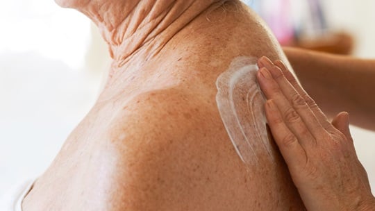 Hand cremt Rücken einer älteren Person ein.