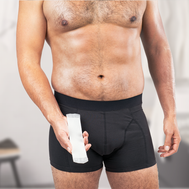 A shirtless man holding a white absorbent pad in his hand while wearing black absorbent underwear.