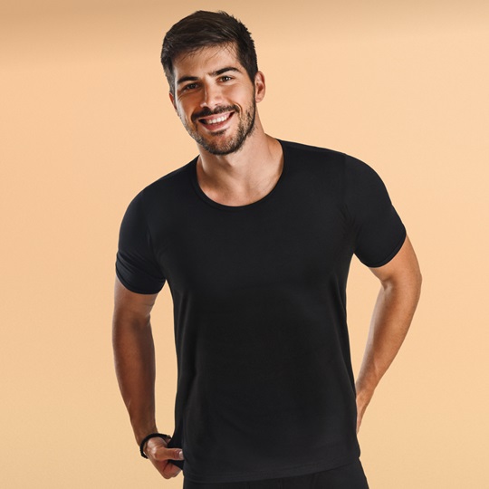 Frontalansicht eines jungen, lächelnden Mannes mit schwarzem T-Shirt und schwarzer, saugfähiger Unterwäsche von MoliCare®.